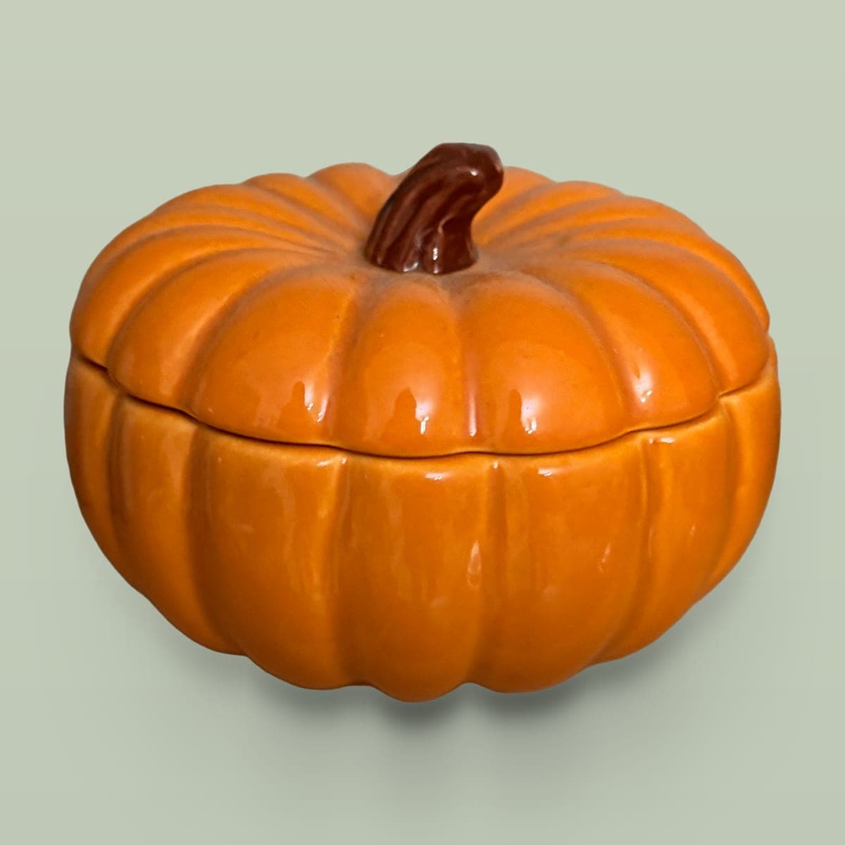 Orange ceramic pumpkin container on a plain sage background with a soft shadow, an Etsy listing photo made in Listzilla Studio