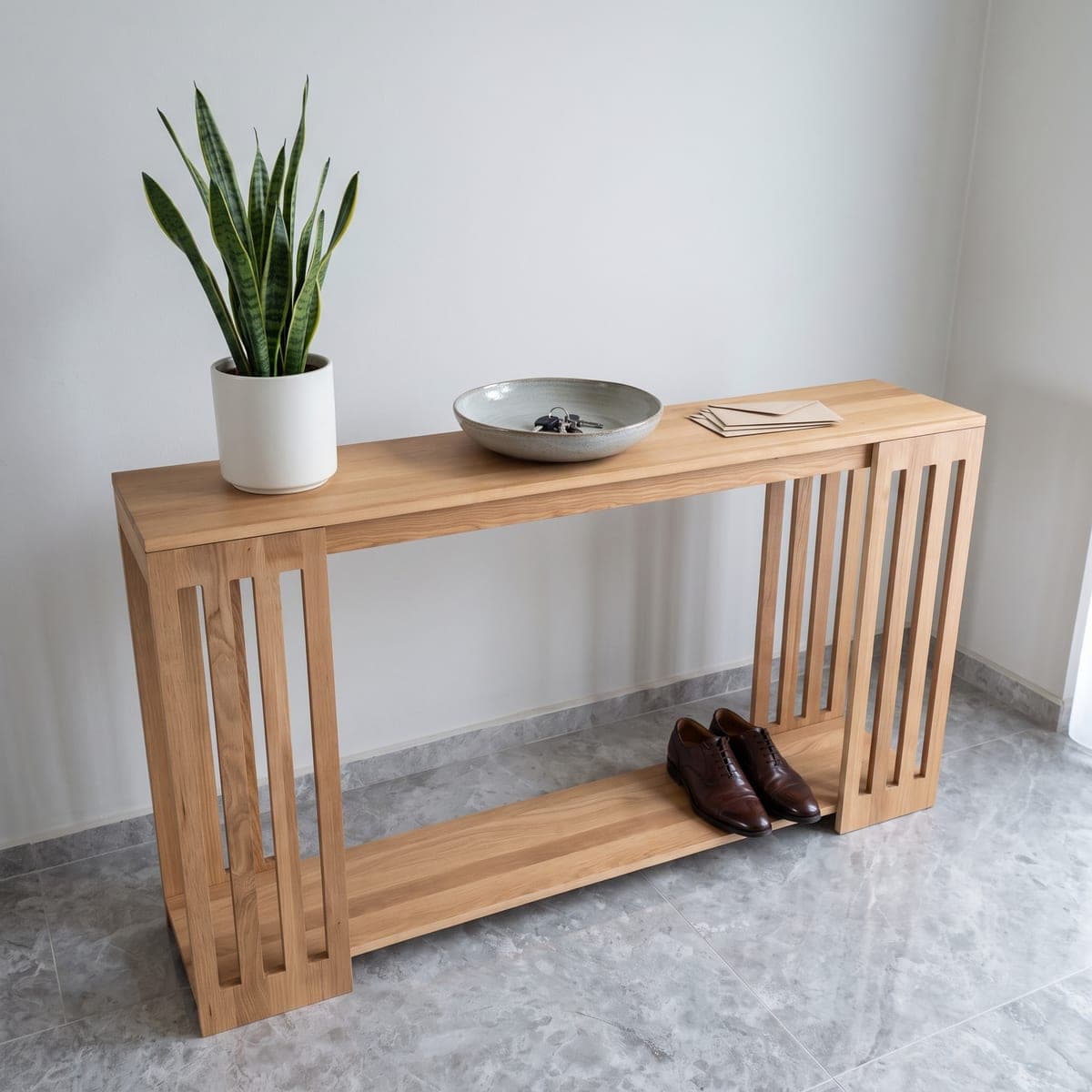 Wooden slatted console table in a bright hallway, with a snake plant and a bowl on top and shoes underneath